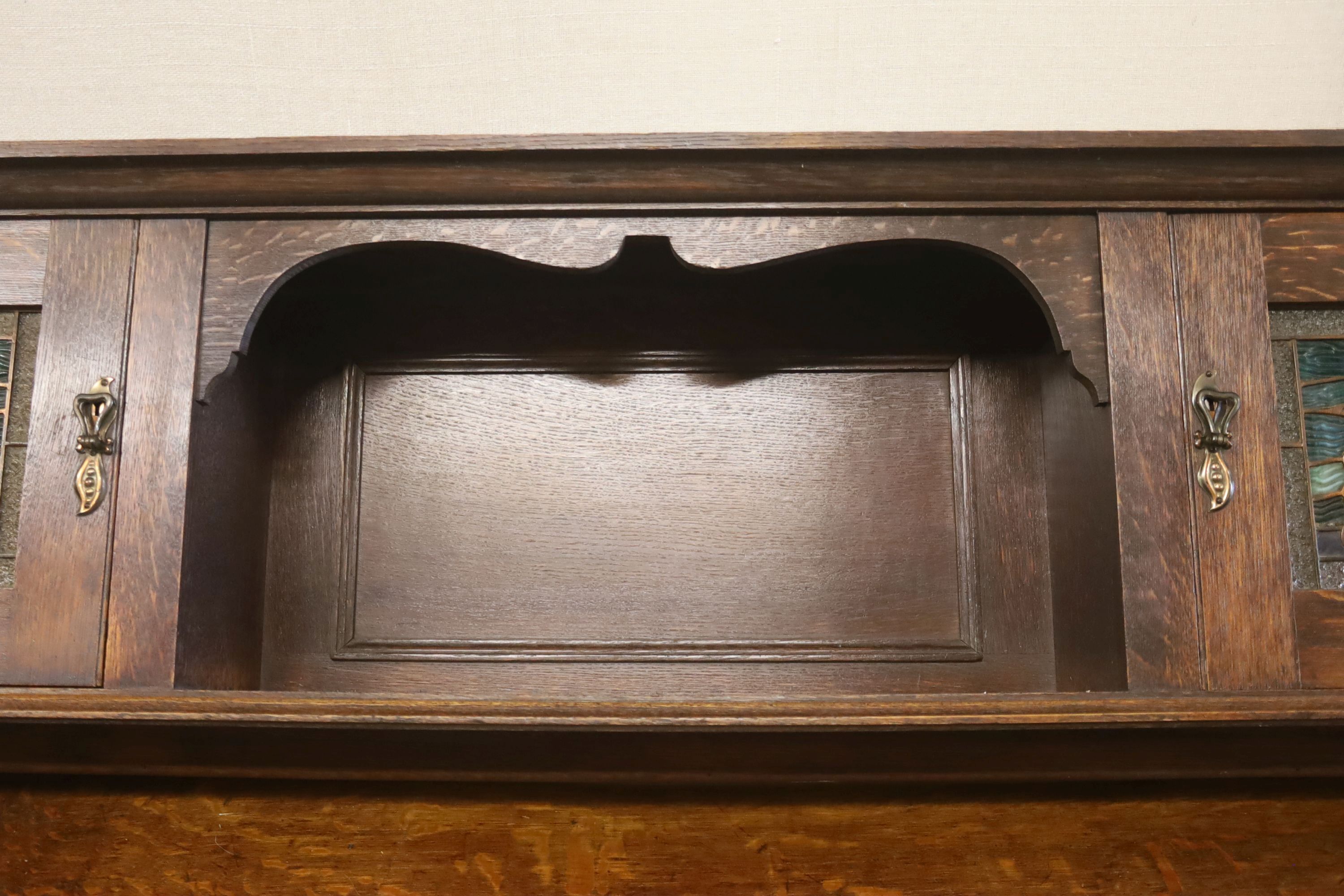 An Arts & Crafts style oak sideboard with stained glass dolphin panels, length 182cm, depth 60cm, height 145cm (lacks top section suppo